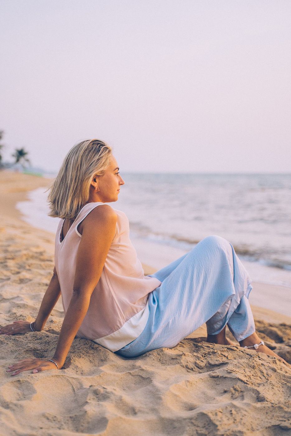 Woman Sitting on the Sandy Shore while Looking Afar